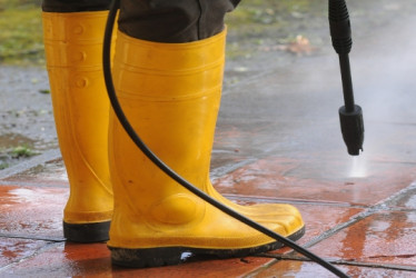 Persona con botas de goma amarillas usando una hidrolavadora en el piso.
