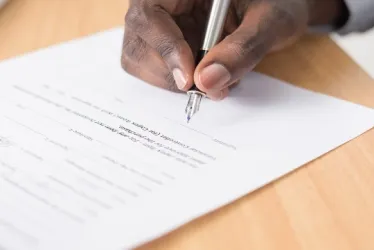 Hombre firma un documento impreso sobre una mesa. 