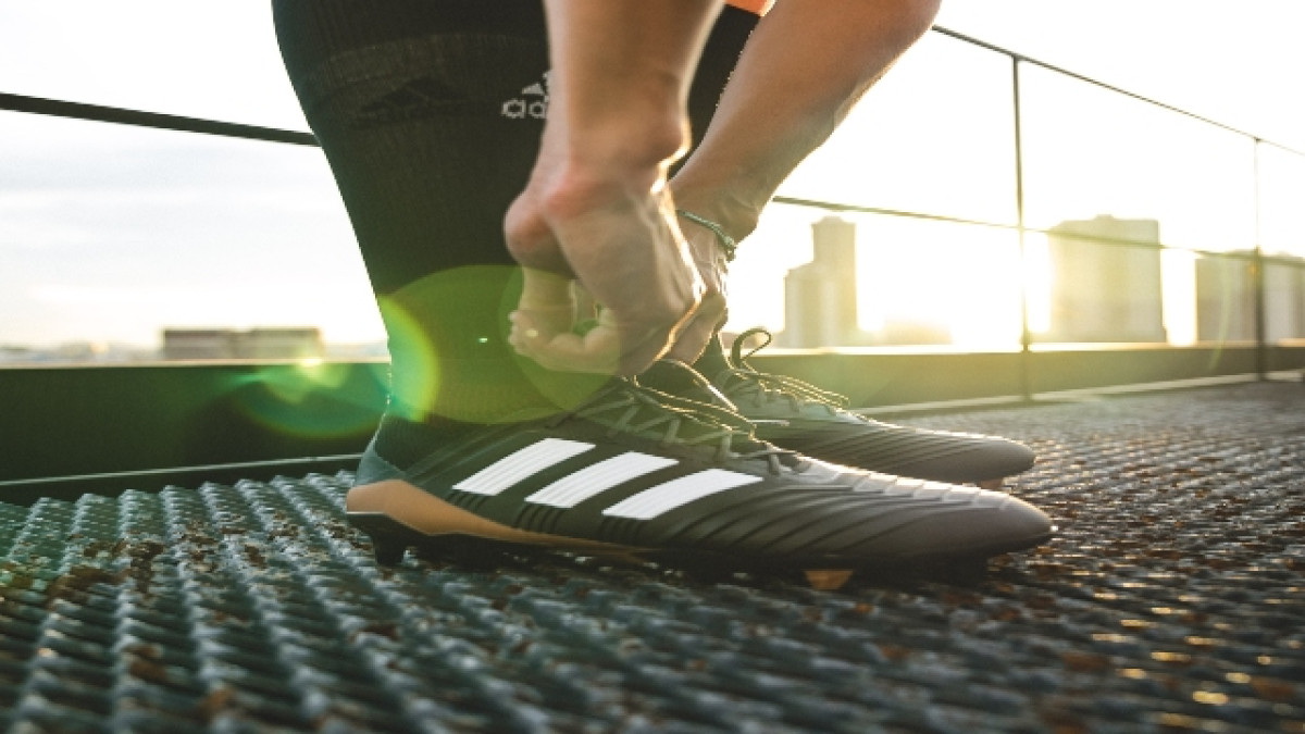 Hombre se amarra los cordones de sus guayos Adidas. 