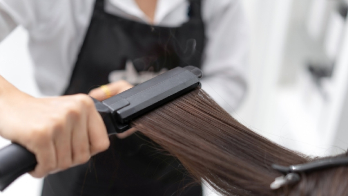 Estilista le plancha el cabello a una mujer.