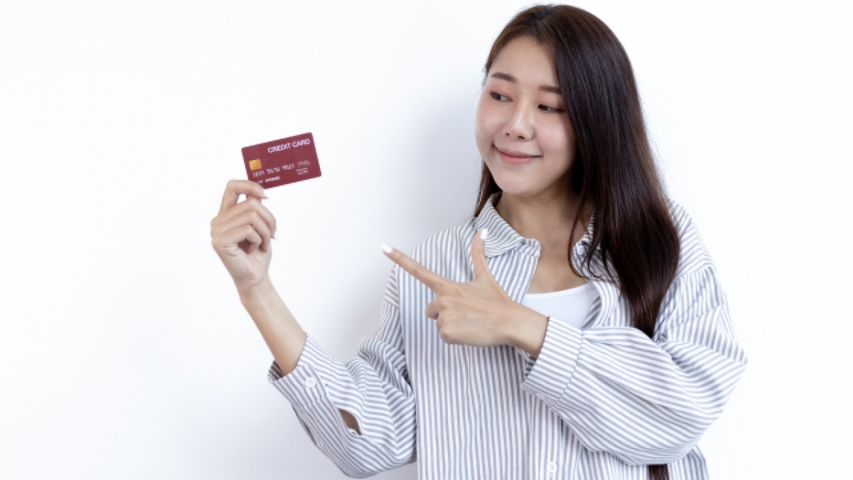 Mujer sostiene una tarjeta de crédito con una mano y la señala con la otra.