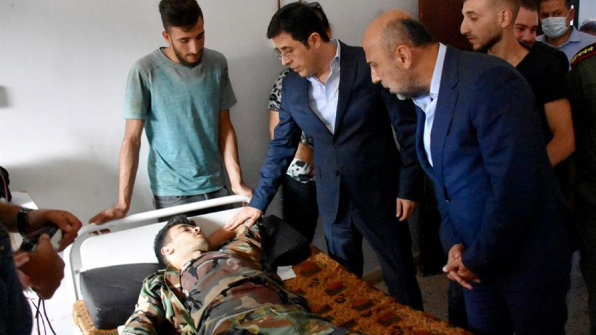 La foto proporcionada por la agencia oficial de noticias árabe siria (SANA) muestra al Ministro de Salud sirio, Hassan al-Ghabash (C), visitando a un herido después de un ataque con aviones no tripulados que tuvo como objetivo una ceremonia de graduación de la academia militar Homs, Siria.