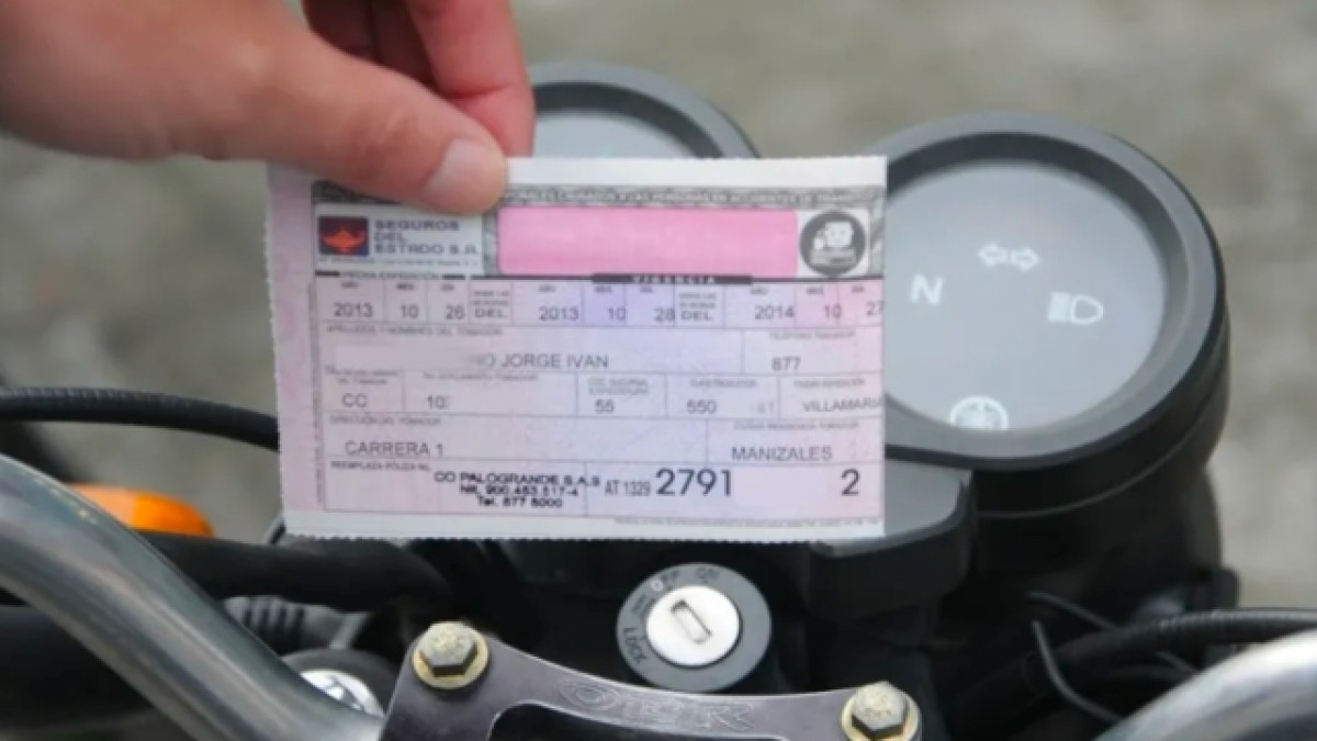 Persona sosteniendo un SOAT frente al tablero de una moto.