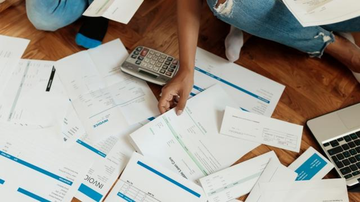 Persona sentada en el piso con facuras y una calculadora.