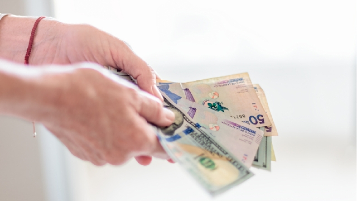 Manos sosteniendo billetes de pesos colombianos y dólares americanos.