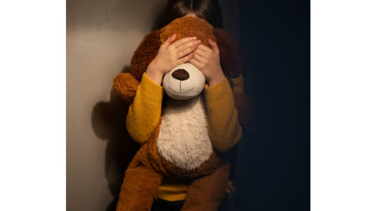 Menor de edad escondida detrás de un oso de peluche