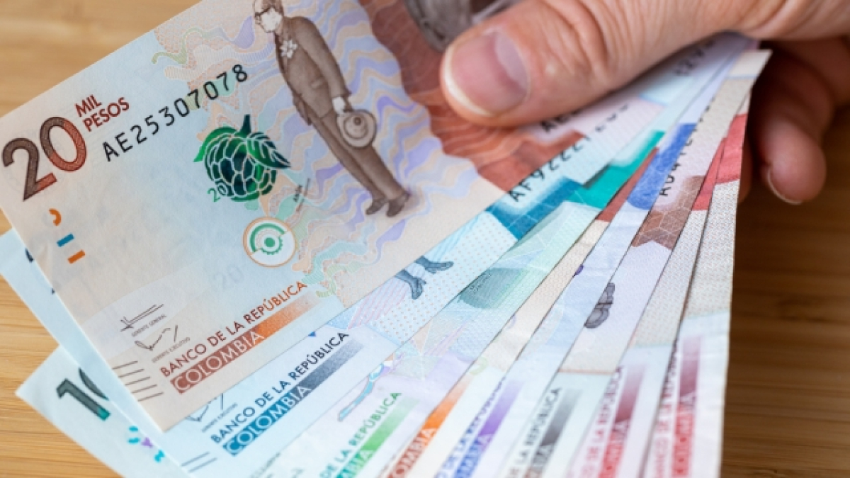 Dedos sosteniendo varios billetes de pesos colombianos