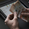 Cuando-se-pagan-los-intereses-de-las-cesantias Dos manos contando billetes de 20 mil pesos colombianos con una tablet en el fondo.