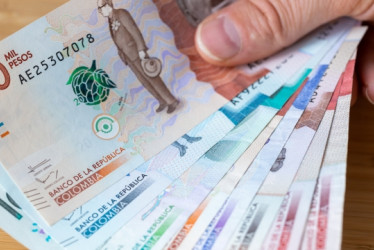 Dedos sosteniendo varios billetes de pesos colombianos