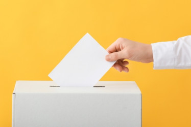 Meno introduciendo un voto en una caja. Fondo amarillo.